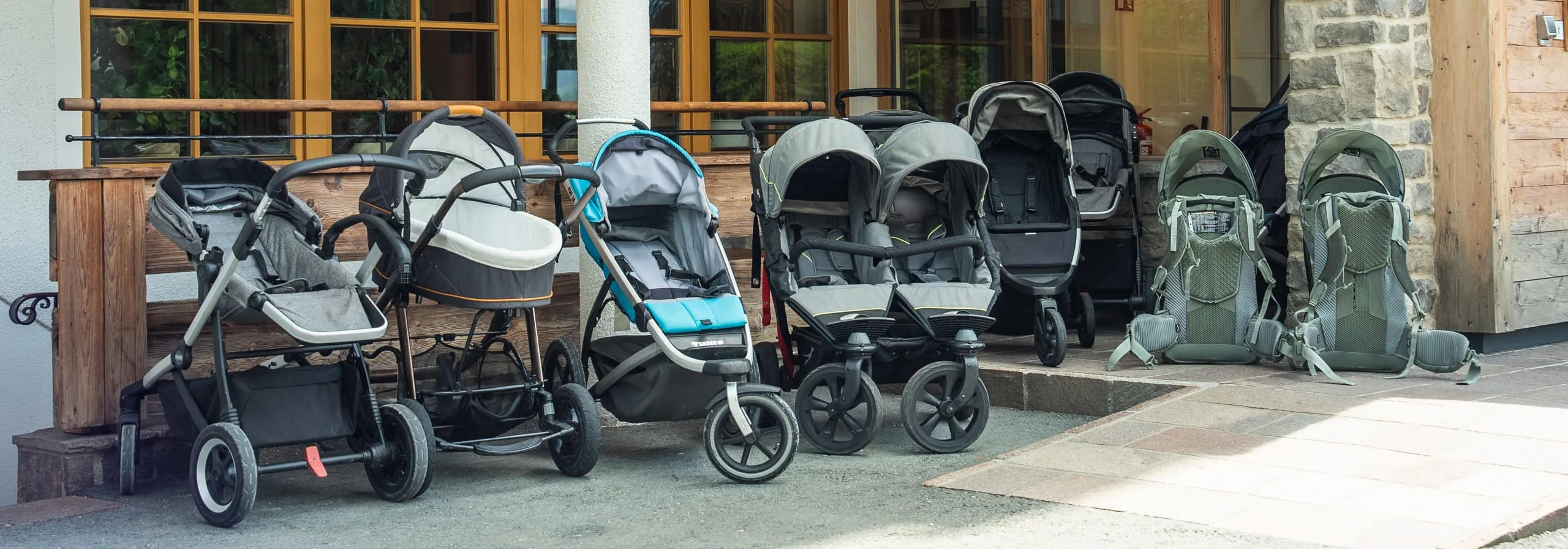 Reihe von verschiedenen Kinderwagen und auch Kindertragerucksack vor dem