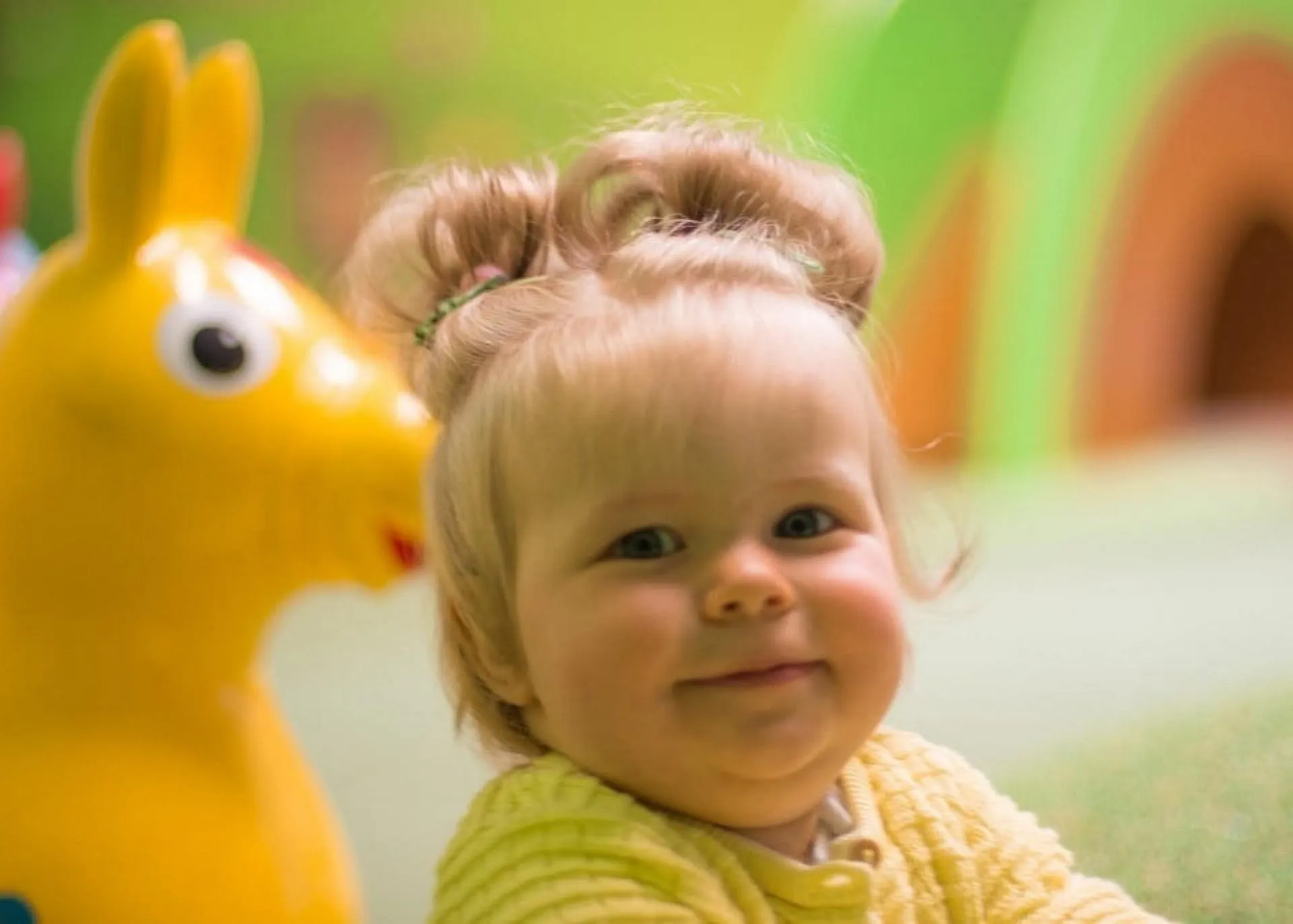 Baby zwischen 0-1 Jahre sitzend vor einem gelben Hüpfpferd