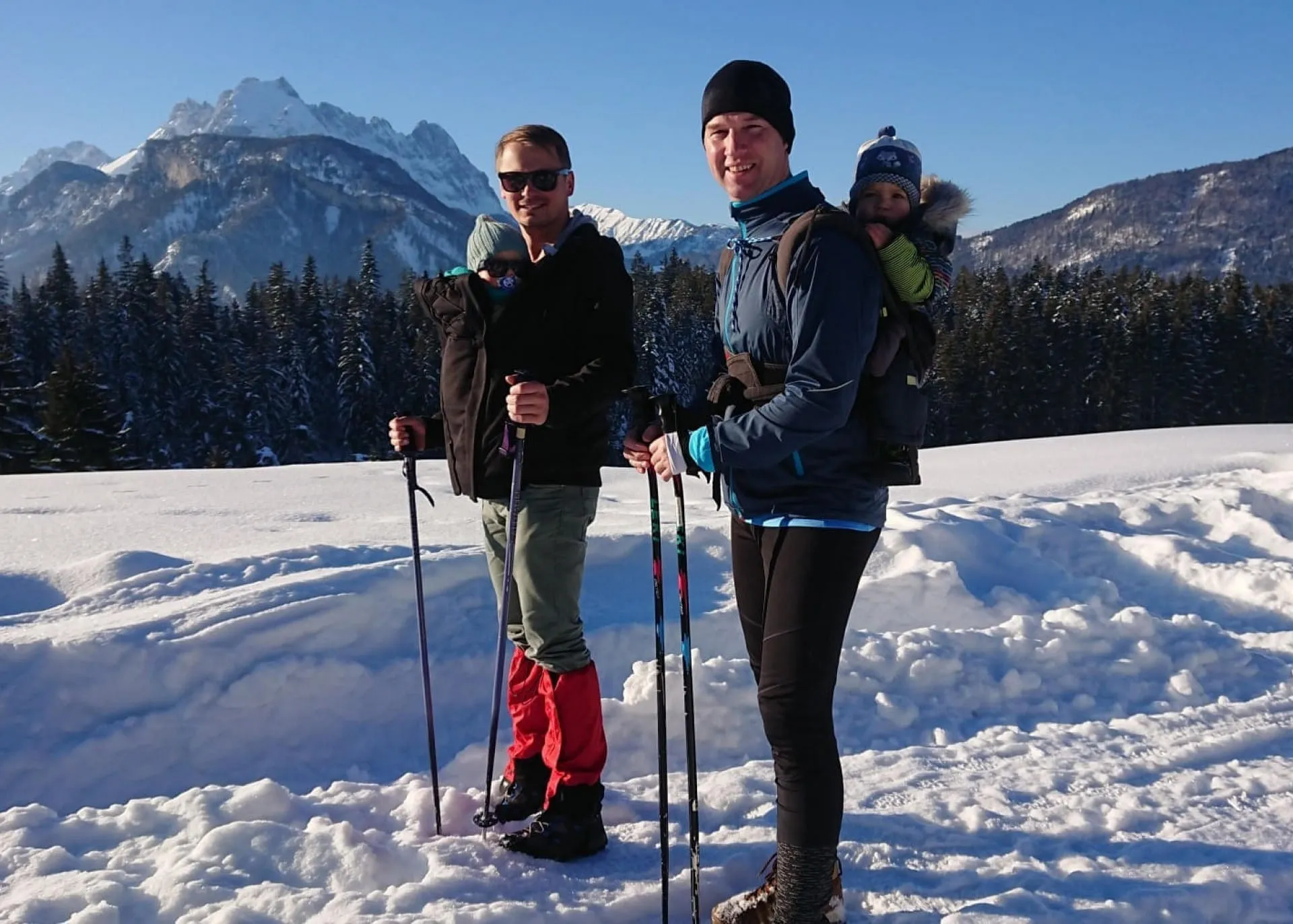 Väter mit Babys in Tragen wandern im Winter durch die verschneiten