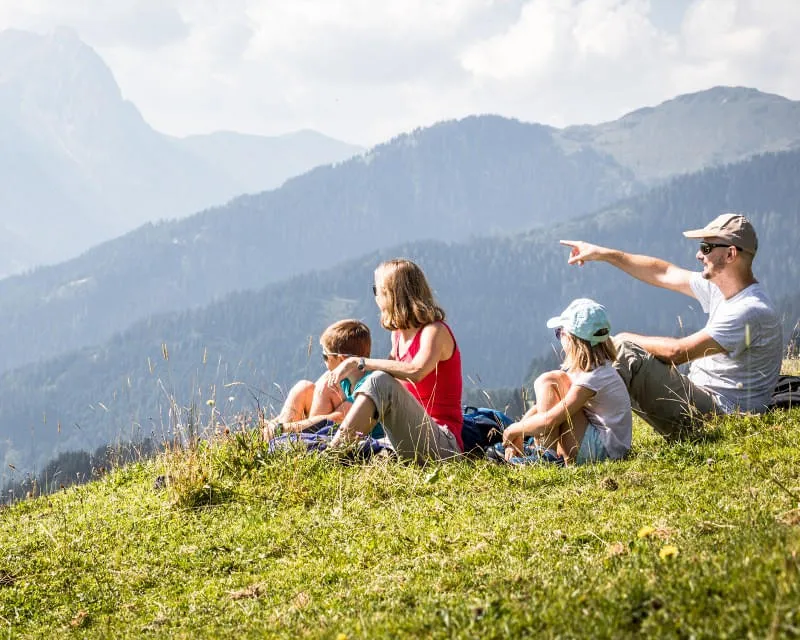 Familie sitzt auf einer Wiese und genießt den Blick auf die Berge der