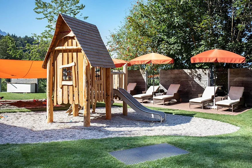 Hotelgarten mit Liegestühlen und Kinderspielplatz mit Holzhaus und Rutsche