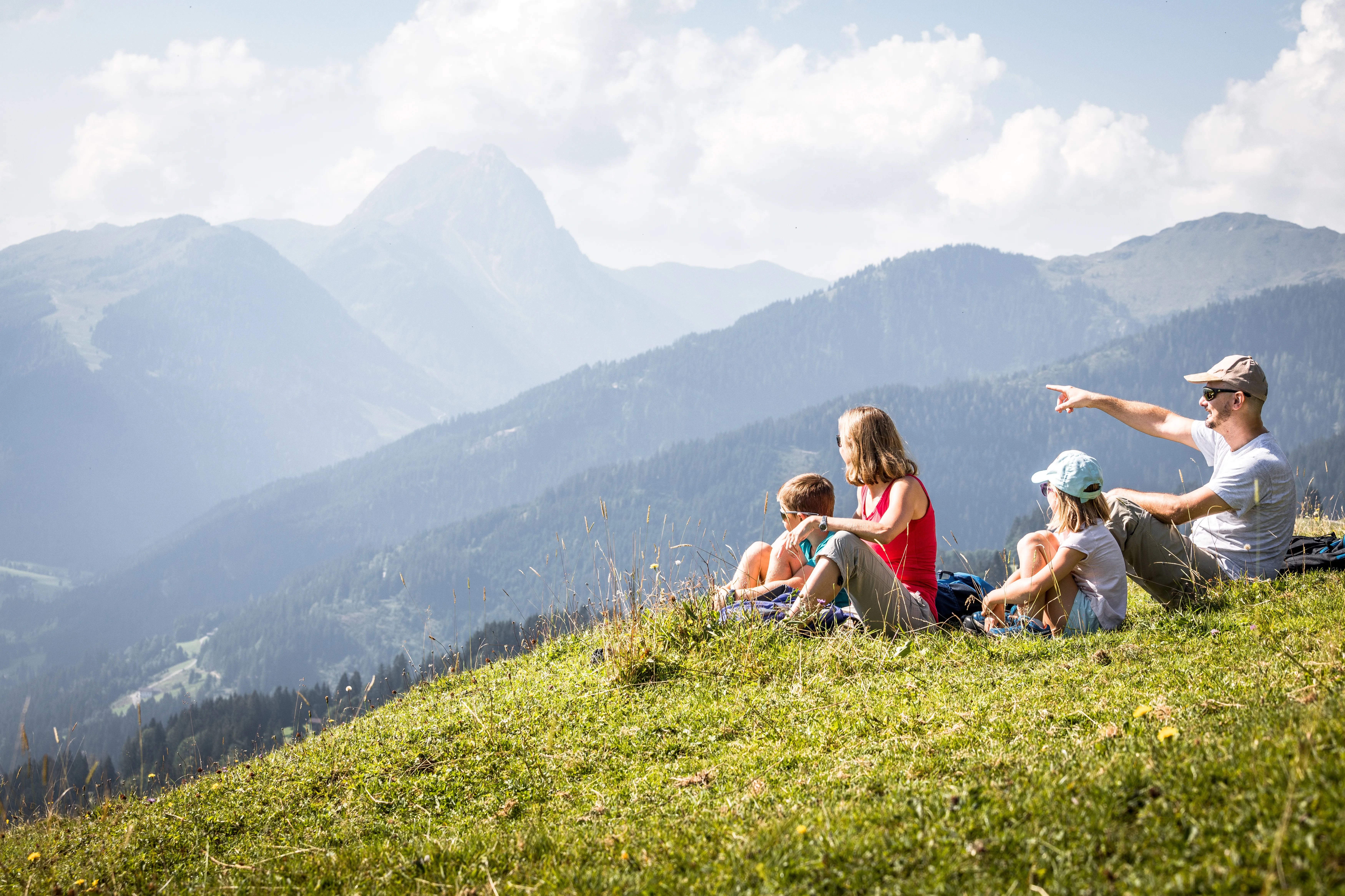 Familie sitzt auf einer Wiese und genießt den Blick auf die Berge der